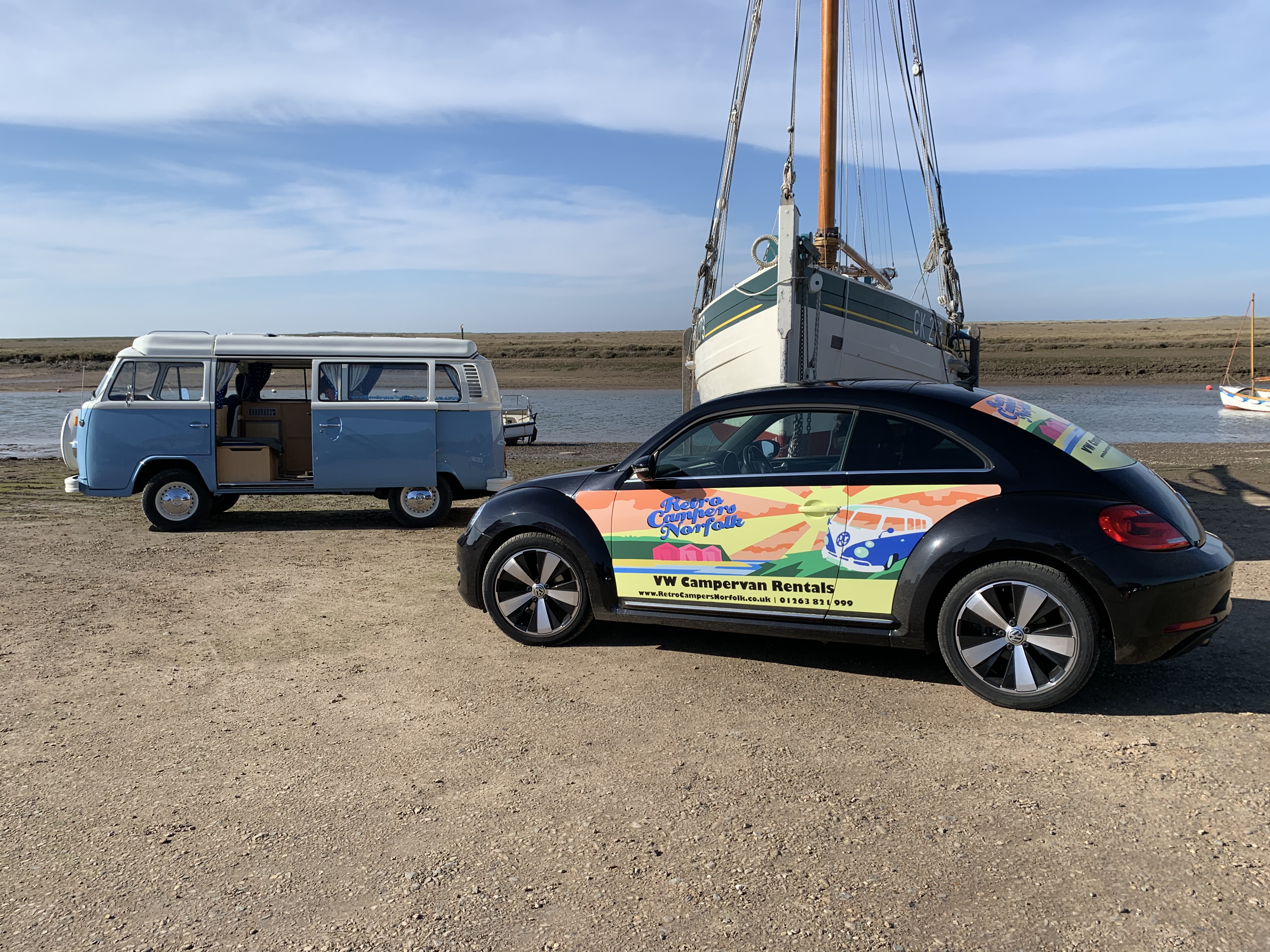 Vintage Blue VW Camper on a dock with a sail boat and beetle